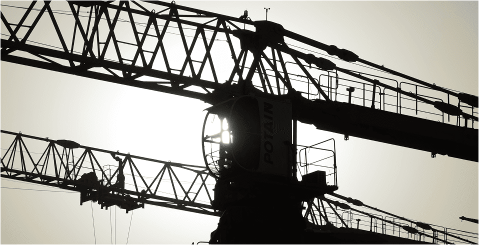 Silhouette of construction cranes against bright sky